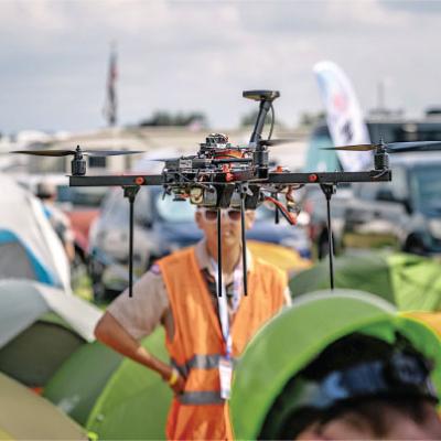 Drone flying over a campsite with tents and people below.