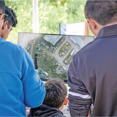 Four people watching a large outdoor screen displaying a map.