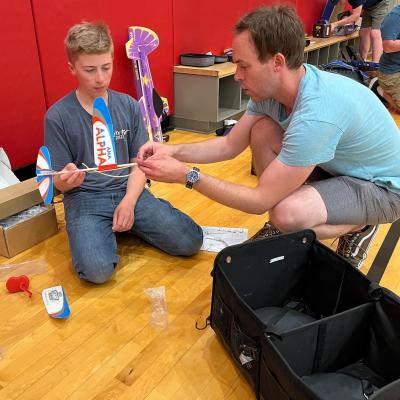Boy and man assembling toy rocket in a gym.