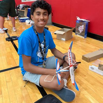 Boy sitting on gym floor with model plane and boxes around.
