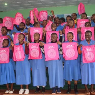 Students in blue uniforms holding pink drawstring bags, smiling.