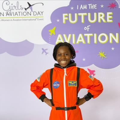 Smiling child in orange astronaut suit at aviation event.