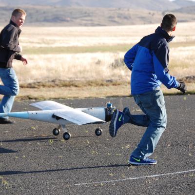 Two young pilots run alongside a model plane.