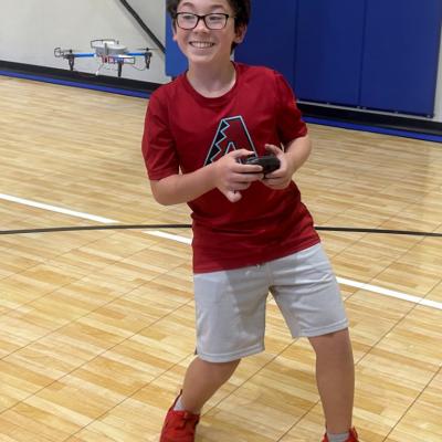 Smiling boy with glasses flying a toy drone in a gym.