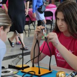 Girl in pink shirt focused on electronics project with tools on table.