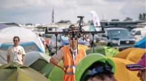 Drone flying over a campsite with tents and people below.