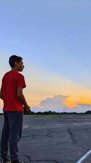Person flying a model airplane at sunset on an open runway.