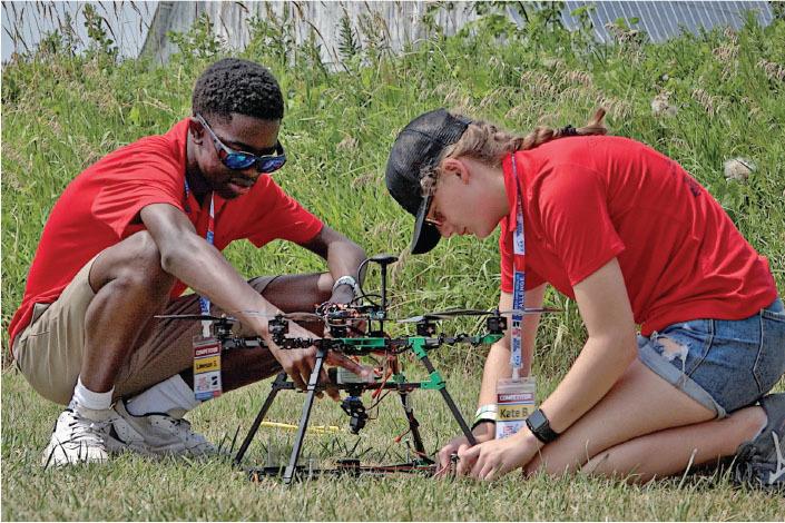Two people in red shirts assembling a small drone outdoors.