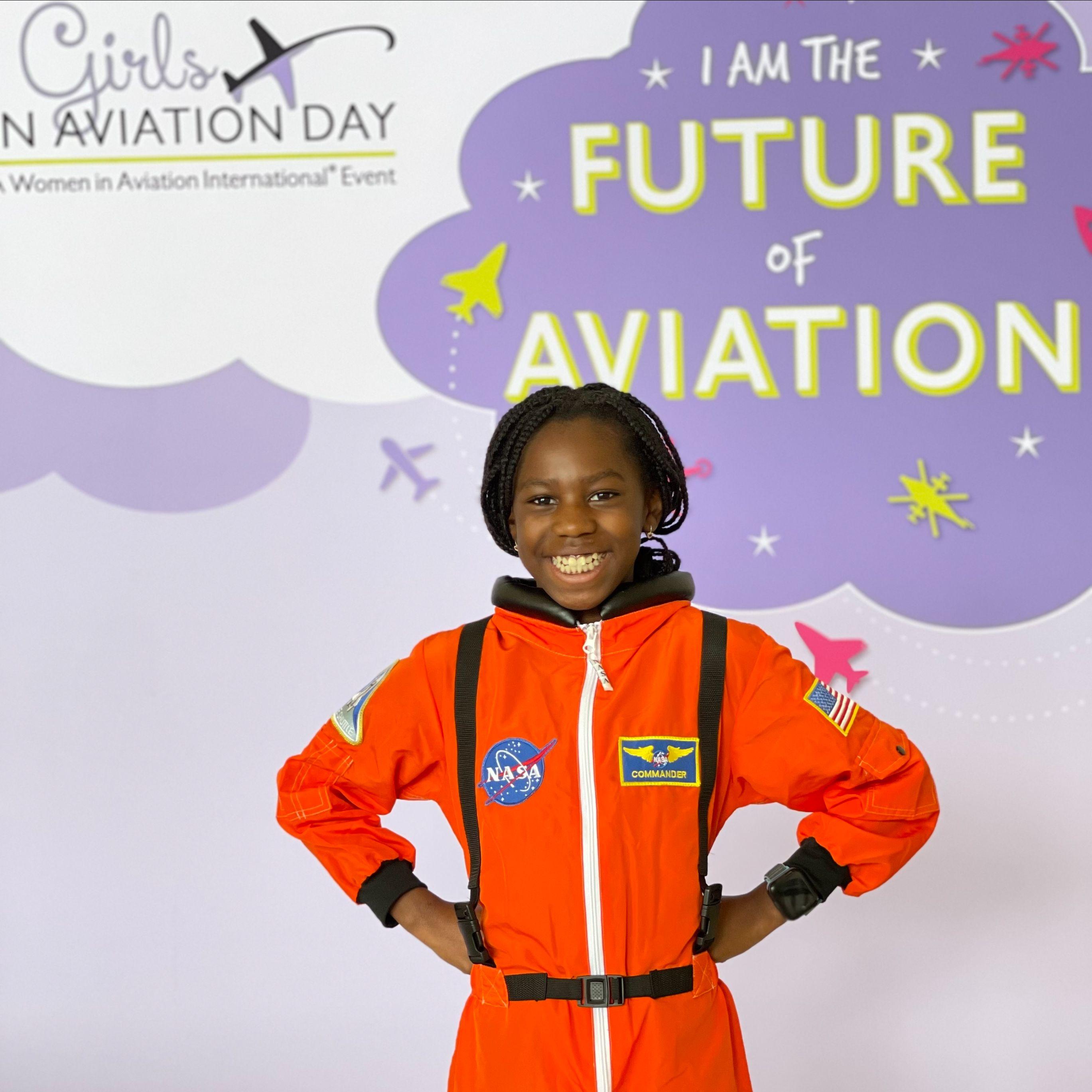 Smiling child in orange astronaut suit at aviation event.