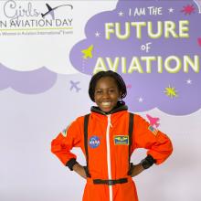 Smiling child in orange astronaut suit at aviation event.